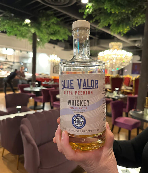Lifestyle shot of Blue Valor Whiskey bottle held in hand with amber color in natural setting