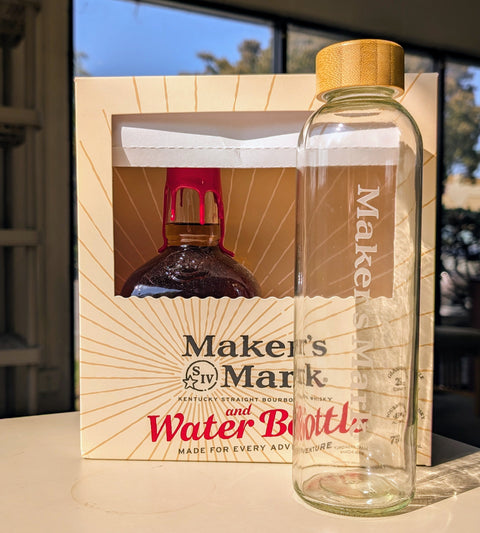 Lifestyle shot of a glass water bottle and gift box with a wooden cap in natural setting.