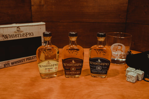Lifestyle shot of three WhistlePig whiskey bottles with decorative caps and a natural background.
